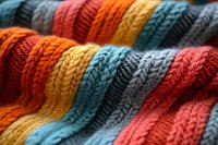 Colorful knitted fabric texture in rainbow stripes pattern. Close up of cozy wool yarn showing detailed stitch structure in orange, blue, yellow, and gray tones.