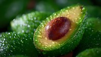 Fresh ripe avocado cut in half showing pit and creamy flesh with water drops on dark green skin, macro food photography for healthy eating concept.
