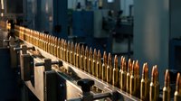 Ammunition production line with copper bullets moving through automated manufacturing equipment in industrial factory setting for defense industry.