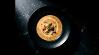 Gourmet bisque soup served in a black bowl on dark marble, topped with seafood and fresh herbs, elegant fine dining presentation.