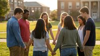 Diverse group of young adults holding hands in circle on college campus during golden hour sunset for teamwork and unity concepts.