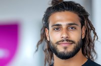 Young mixed race man with dreadlocks and beard smiling confidently against blurred background. Modern casual style portrait showing genuine positive expression.