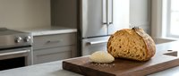 Freshly baked artisan bread loaf sliced on wooden cutting board in modern kitchen with stainless steel appliances and natural light.