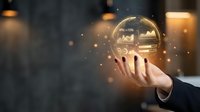Businessman hand holding glowing crystal ball with financial charts and data analytics for future business forecasting and strategic planning.