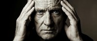 Stressed elderly Caucasian man holding head in hands showing mental health struggles and emotional pain in dramatic black and white portrait.
