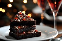 Rich chocolate brownie layers with caramel filling and red candy decorations on white plate, festive bokeh lights background creates romantic dessert atmosphere.
