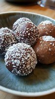 Homemade chocolate truffles rolled in coconut flakes and cocoa powder served on rustic blue ceramic plate, close-up view of gourmet confectionery dessert.