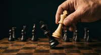 Male hand moving white king chess piece on wooden chessboard with black pieces in background, strategic business concept for leadership and decision making.