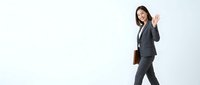Young Asian female professional in dark business suit and brown leather briefcase waving greeting gesture against white background for corporate communications.