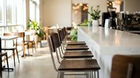 Modern cafe interior with white counter, brown leather bar stools, and natural light from windows. Ideal for restaurant, hospitality, and commercial design projects.
