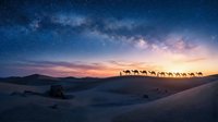 Camel caravan silhouettes crossing desert dunes under starry Milky Way galaxy at twilight with colorful sunset sky creating magical landscape scene.