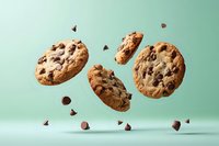 Freshly baked chocolate chip cookies floating in air with scattered chocolate chips against mint green background, levitation food photography style.