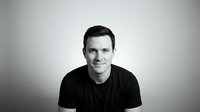 Young adult male with dark hair and fair complexion wearing black t-shirt against neutral gray background, suitable for corporate profiles, business websites, and professional headshot collections.