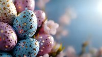 Speckled pastel Easter eggs in blue and pink with gold glitter accents against soft spring blossoms and dreamy bokeh background for holiday celebrations.