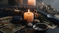 Mystical fortune telling setup with burning candles, tarot cards, crystal ball and dried herbs creating atmospheric divination scene for spiritual guidance.