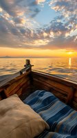 Cozy wooden boat at sunset with comfortable pillows and blanket, sailing on calm ocean waters under dramatic golden sky with sunlit clouds.