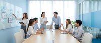 Business team meeting in modern conference room with diverse professionals discussing strategy and collaboration around wooden table.