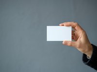 Male hand holding blank white business card against gray background, suitable for branding, corporate identity, and marketing mockup designs.