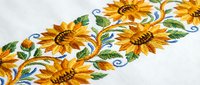 Embroidered sunflower border on white linen fabric with decorative swirls and green leaves for textile design and craft projects.