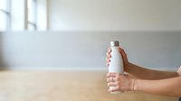 Close-up of hand holding white spray bottle against neutral interior background, suitable for cleaning product marketing and household care advertising.