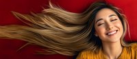 Young Asian woman with flowing blonde hair smiling with closed eyes against red background, wearing yellow sweater. Natural beauty and happiness concept for wellness and lifestyle.