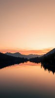Serene mountain lake at sunrise with golden sky reflecting on calm water, surrounded by evergreen forest silhouettes and distant peaks for nature and travel projects.