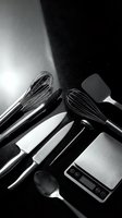 Modern kitchen utensils and digital scale arranged on dark surface in dramatic black and white photography for culinary design projects.