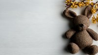 Brown knitted bunny toy with yellow autumn leaves on white wooden background, copy space for seasonal greetings or nursery decoration.