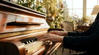 Hands playing wooden piano keys in warm sunlight streaming through window with plants creating peaceful musical moment for relaxation and creativity.