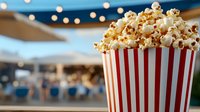 Fresh popcorn overflowing in striped container against blurred festive background with bokeh lights, capturing entertainment and movie night atmosphere.