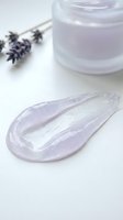 Lavender-infused gel cream with shimmering texture displayed on white surface alongside dried lavender flowers and open jar for skincare and cosmetic product marketing.