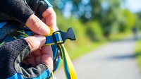 Close-up of hiker's hands adjusting backpack strap buckle on sunny outdoor trail, preparing for adventure and outdoor recreation activities.
