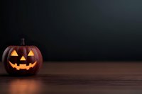 Glowing carved pumpkin with classic jack o'lantern face on dark wooden surface against black background, creating spooky Halloween atmosphere.