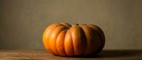 Large orange pumpkin with deep ridges sitting on rustic wooden surface against neutral background for autumn harvest seasonal decoration.