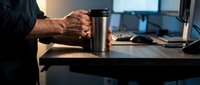Professional businessman holding coffee mug at modern office desk with laptop and documents during evening work session for productivity concepts.