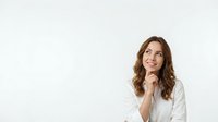 Young professional woman with brown wavy hair in white blazer looking up thoughtfully with hand on chin, isolated on white background for business design.