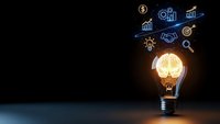 Glowing light bulb with business icons floating above on dark background representing innovation, creativity and entrepreneurial success in corporate strategy.