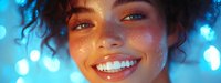 Young mixed race woman with curly hair smiling broadly showing white teeth against blue bokeh lights background, face close-up with glowing freckled skin and bright eyes.