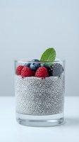 Chia seed pudding topped with fresh raspberries, blueberries, and blackberries, garnished with mint leaf in glass on white background for healthy dessert and breakfast content.