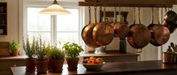 Rustic farmhouse kitchen with hanging copper pots, fresh herb plants in terracotta pots, and a wooden countertop in warm natural light.