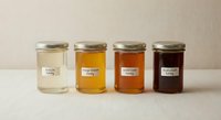 Four glass jars containing different grades of honey from light to dark amber, showcasing natural sweetener varieties for culinary and gourmet food uses.