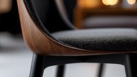 Close-up detail of modern dining chair with curved wooden backrest and black leather upholstery against blurred background, showcasing contemporary furniture design.