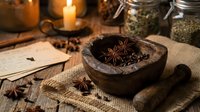 Rustic wooden mortar and pestle with star anise and spices on burlap, surrounded by glass jars, candles and recipe cards creating cozy kitchen atmosphere.