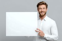 Smiling man in white shirt holding blank sign against gray background, pointing to empty space for your message or advertisement.