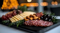 Appetizing charcuterie board with sliced salami, cheese, almonds, olives and fresh rosemary garnish on dark slate plate against blurred bokeh lights background.