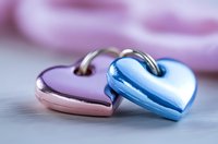 Two metallic heart-shaped padlocks in pink and blue colors interlinked together on blurred background, romantic symbol of eternal love and commitment.
