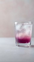Refreshing purple gradient cocktail with ice cubes in clear glass on neutral background for beverage and lifestyle concepts.