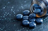 Shimmering blue pills spilling from glass jar on dark textured surface with bokeh effect background, dramatic pharmaceutical composition for medical concepts.