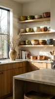 Modern kitchen interior with wooden floating shelves displaying colorful ceramic bowls and copper cookware in warm natural sunlight.