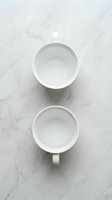 Two empty white ceramic coffee cups on marble surface viewed from above for kitchen and cafe branding projects.
